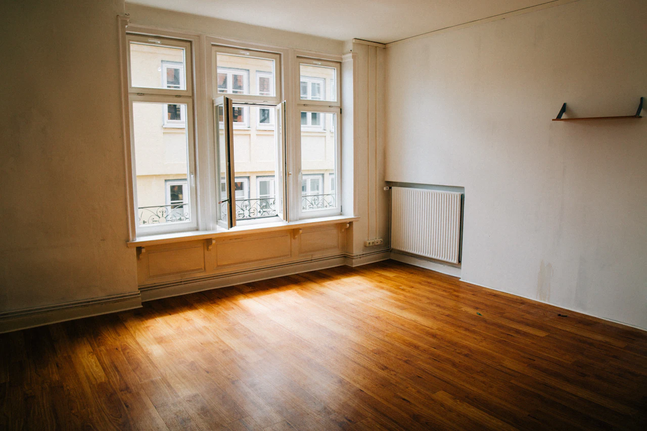 Lege kamer met houten vloer en een rij ramen in het zonlicht