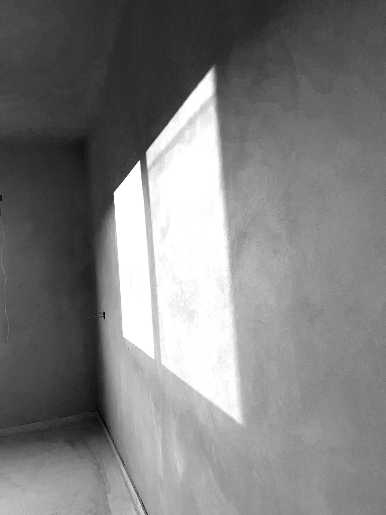 Zonlicht valt door een raam op een gladde, grijze pleistermuur
